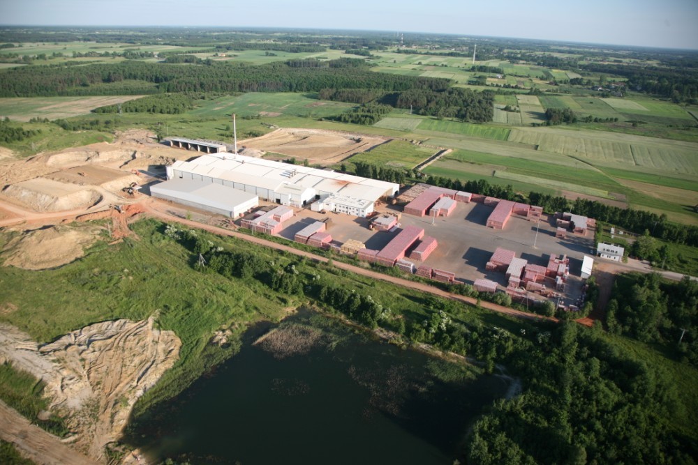 Widok z lotu ptaka. Duże budynki z białymi dachami, dookoła zielone lasy i pola