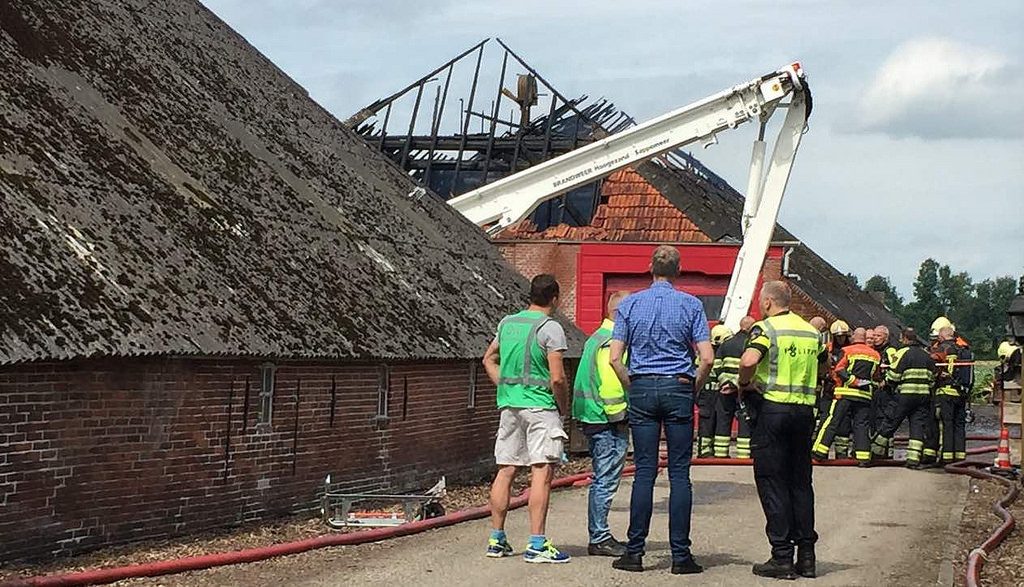 stary budynek pokryty eterniktem i kilka osób w roboczysz strojach. w tle podnośnik
