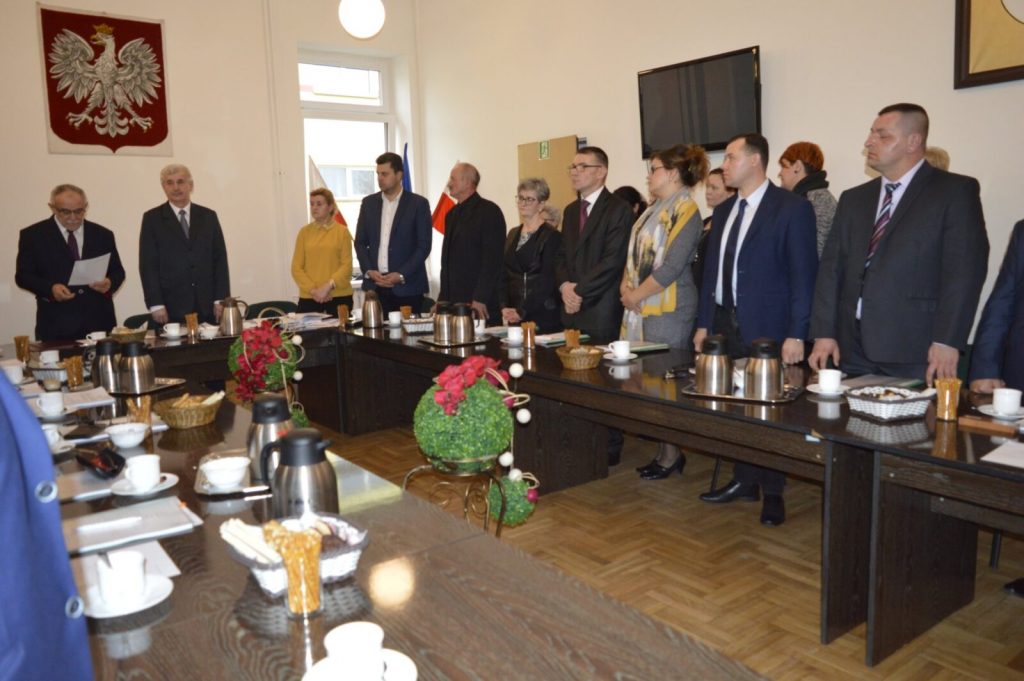 ludzie stojący przy stołach. Naścianie godło Polski.