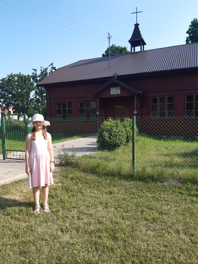 Dziewczynka przed drewnianą kaplicą.