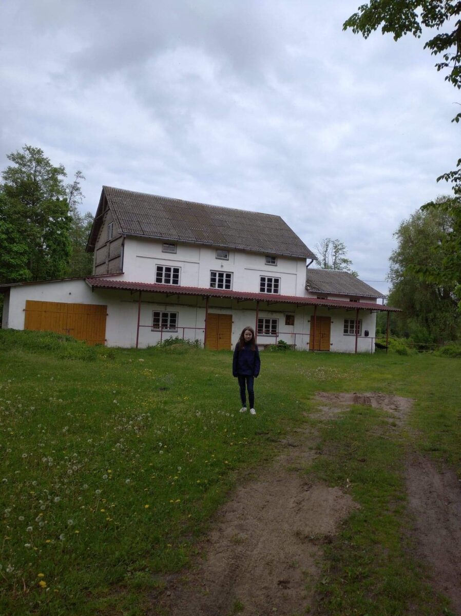 Kilkunastoletnia dziewczynka na tle białego budynku.