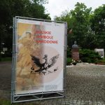Plansza wystawowa z napisem "Polskie Symbole Narodowe", w tle park
