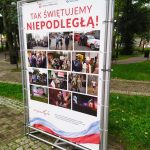 Plansza wystawowa z napisem "Tak świętujemy Niepodległą", w tle park