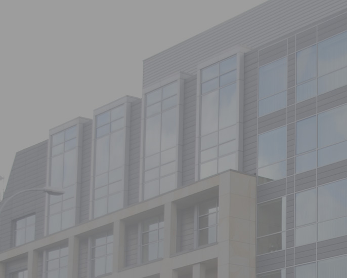 Przeszklony szczyt budynku z onami i szarą elewacją, w tle błękitne niebo