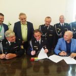 Trzech mężczyzn siedzących przy czarnym stole, za nimi stoi pięciu mężczyzn