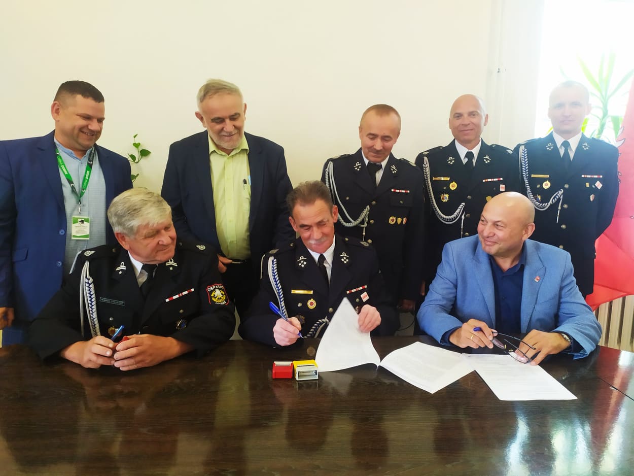 Trzech mężczyzn siedzących przy czarnym stole, za nimi stoi pięciu mężczyzn