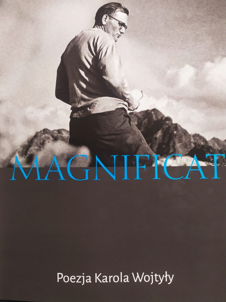 Mężczyzna w okularach. Widoczny napis - niebieskimi literami - Magnificat