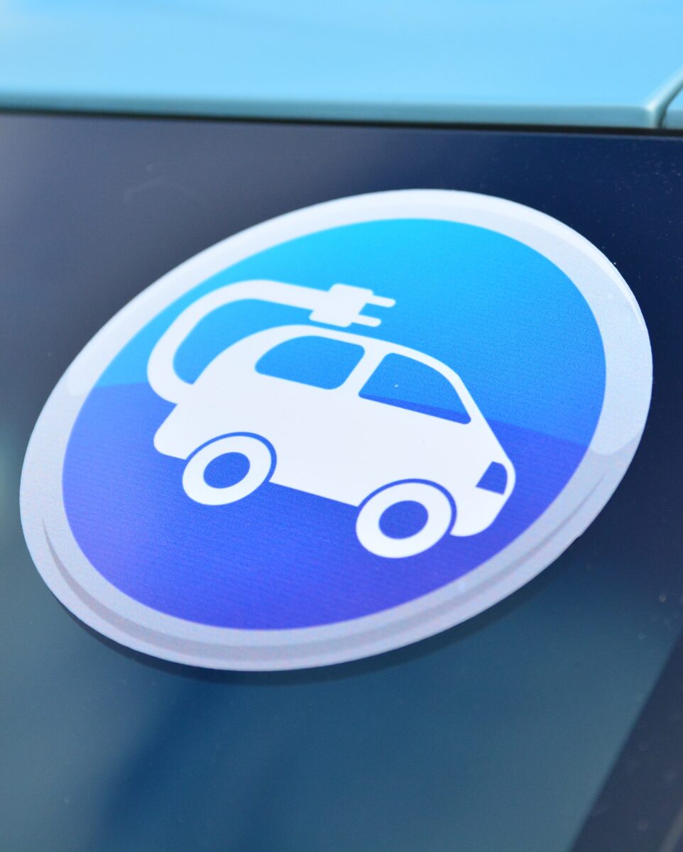 Nalepka na samochodzie, przedstawiająca. piktogram samochodu z wtyczką elektryczną.