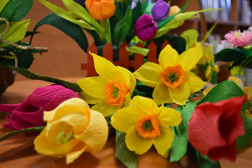 Żółte i kolorowe kwiaty W tle mały czerwony płotek z kolorowymi kwiatami