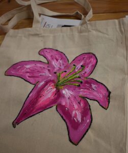 Na płóciennej torbie namalowana jest lilia w różnych odcieniach różu i żółtym środkiem