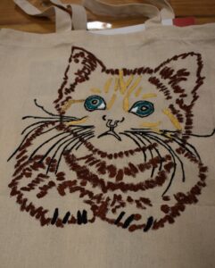 Na płóciennej torbie kotek namalowany w kolorze brązowym z zielonymi oczami.