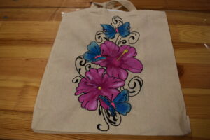 Na drewnianym stole leży płócienna torba na której są namalowane różowe kwiaty i niebieskie motyle
