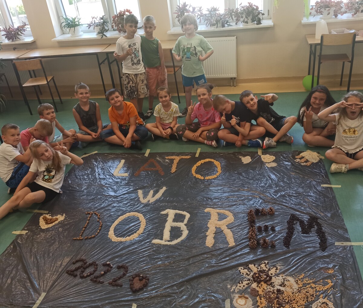W sali dzieci siedzą przy napisie Lato w Dobrem.