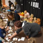 Grupa przedszkolaków i dwie panie pozują do zdjęcia. Dzieci w rękach trzymają kolorowe misie. W tle czarna kotara z białym napisem i gwiazdkami, przed nimi leżą kolorowe poduszki