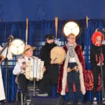 Kilka osób na scenie, z lewej strony dziewczyna grająca na gitarze.