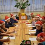 Dzieci siedzące przy drewnianym stole w czerwonych czapkach