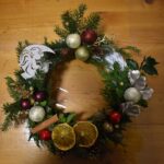 415 Wianek z jodły, świerku, złotych i czerwonych bombek, pomarańczy, cynamonu, drewniana figurka aniołka zdobi go.