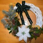 423 Biały wianek ratanowy z jodły, świerku, pomarańczy, cynamonu, orzecha pomalowanego na złoto, bombki czerwone i srebrne. Na górze kokarda czerwono zielona w kratkę.