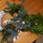 435 Duży wianek ozdobiony złotymi i bordowymi bombkami, pomalowanymi na złoto orzechami, pomarańczami. U góry widać fragment białego ratanowego wianka.