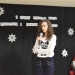 163 Nastolatka w czarnej sukience trzyma mikrofon. w tle czarna kotara z gwiazdkami i białym napisem.