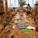 174 Chłopcy stoją przy stole który jest posypany maka, jeden z nich zagniata ciasto.