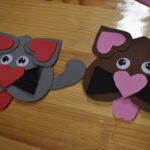 183 Dzieci stoją wokół stołu na którym stoją naczynia z ciastem, wędliną, olejem i leżą deski do krojenia z nożami. Kobieta z jednym z chłopców ugniata ciasto w blaszce.