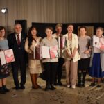 Osiem kobiet i dwóch mężczyzn stoi w półkolu, kobiety trzymają w reku dyplomy.