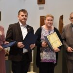 Grupa 4 osób stojących obok siebie - dwie kobiety i dwóch mężczyzn. Jedna z kobiet trzyma dyplom.