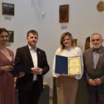 Grupa 4 osób stojących obok siebie - dwie kobiety i dwóch mężczyzn. Jedna z kobiet trzyma dyplom.