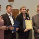 Cztery kobiety i dwóch mężczyzn. Jedna z kobiet trzyma dyplom.Troje dorosłych oraz troje dzieci. Stoją obok siebie. Dziewczynka trzyma dyplom.