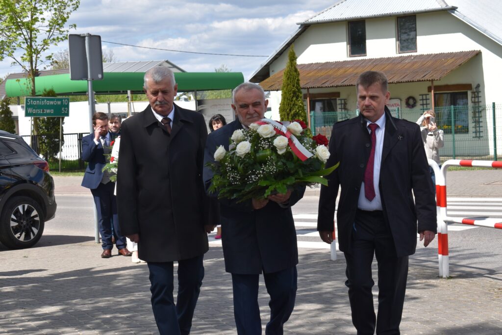 Trzech mężczyzn, jeden z nich trzyma wiązankę kwiatów.