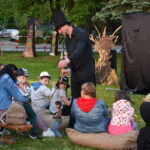 Kilkanaście osób siedzących na trawie