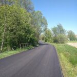 Droga asfaltowa, z lewej strony ogrodzenie.