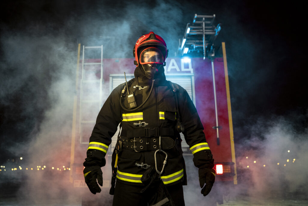 strażak w pełnym umundurowaniu stojący przed pojazdem strażackim