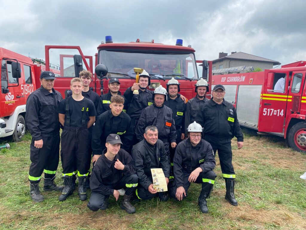 Grupa kilkunastu osób - strażaków na tle samochodu