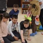 Na zielonym dywanie stoi kula a dzieci siedzące w kole dotykają ją rękoma