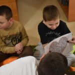 Na zielonym dywanie stoi kula a dzieci siedzące w kole dotykają ją rękoma