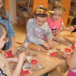 Dzieci w Bibliotece na drewnianym stole zabierają się do pieczenia pierników. W tle regały z książkami