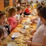 Dzieci w Bibliotece na drewnianym stole zabierają się do pieczenia pierników. W tle regały z książkami