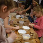 Dzieci w Bibliotece na drewnianym stole zabierają się do pieczenia pierników. W tle regały z książkami