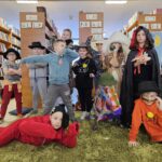 266 Rozbawione dzieci i poprzebierane bawią się na zielonym dywanie w tle regały z książkami