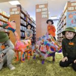 267 Czterech chłopców przebranych z podróżników i kolorowe makiety dzika i smoka. W tle regały z książkami