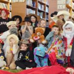 267 Uczestnicy zajęć na feriach poprzebierani w kolorowe stroje pozują na tle regałów z książkami do zdjęcia