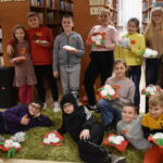 106 W bibliotece stoją dzieci i trzymają w rękach kwiaty które zrobili na prezent dla la swoich Babć .