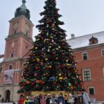 148 Dzieci pozują do zdjęcia za nimi stoi duża choinka ubrana kolorowym bombkami i łańcuchami. W tle Zamek królewski