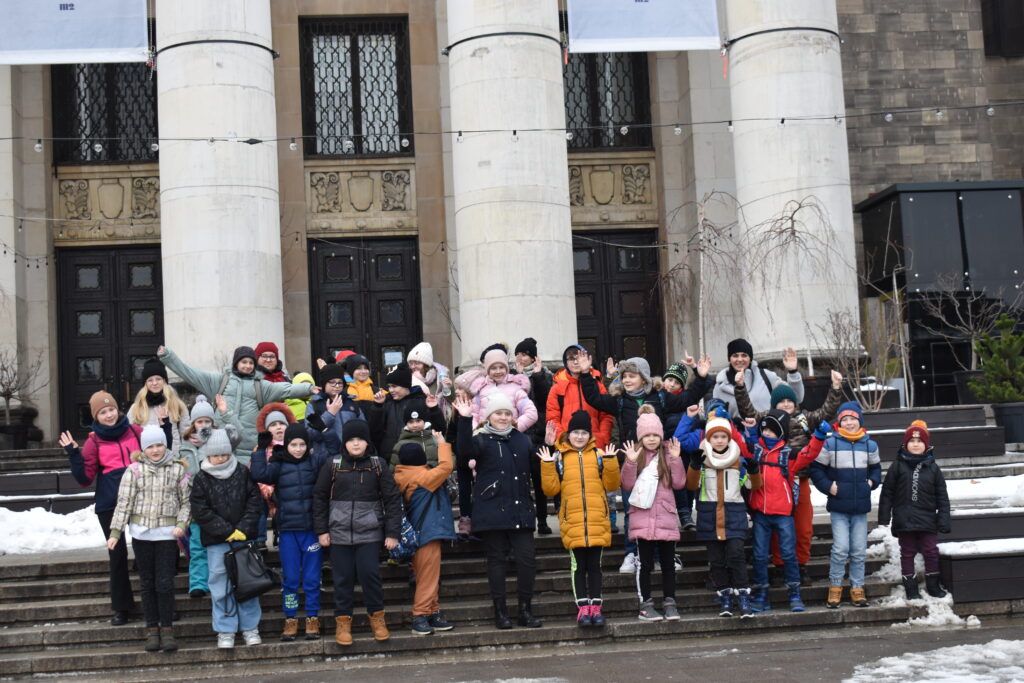 173 Grupka zadowolonych dzieci macha rękoma. W tle kolumny budynku