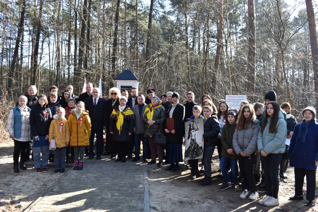 Na zdjęciu widać grupę ludzi, która stoi na terenie zalesionym. Przyrodniczy krajobraz powodujący zagrożenie dla ich spotkań lub spaceru.