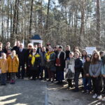 Na zdjęciu widać grupę ludzi, która stoi na terenie zalesionym. Przyrodniczy krajobraz powodujący zagrożenie dla ich spotkań lub spaceru.