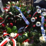 Na obrazku widocznym jest wieniec z czerwonych, białych i niebieskich kwiatów. Jest on starannie wykorzystany i zawiera różnorodne kształty i odcienie, dodając do niego głębię i różnorodność kolorów.