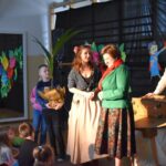 Na otwartej przestrzeni jest grupa osób dorosłych stojących przed zestawieniem dzieci. Wydaje się, że wszyscy są skupieni na odrębnym zdarzeniu lub aktywności.